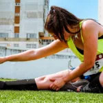 Hardloopster met zwarte compressiekousen rekt haar been op het gras voor een loopwedstrijd, compressiekousen hardlopen
