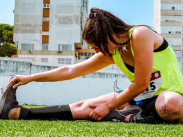 Hardloopster met zwarte compressiekousen rekt haar been op het gras voor een loopwedstrijd, compressiekousen hardlopen