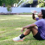 Hardloper drinkt water in het gras na een loop om vocht en elektrolyten aan te vullen