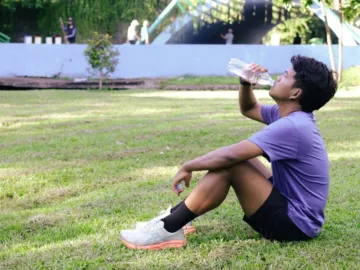 Hardloper drinkt water in het gras na een loop om vocht en elektrolyten aan te vullen