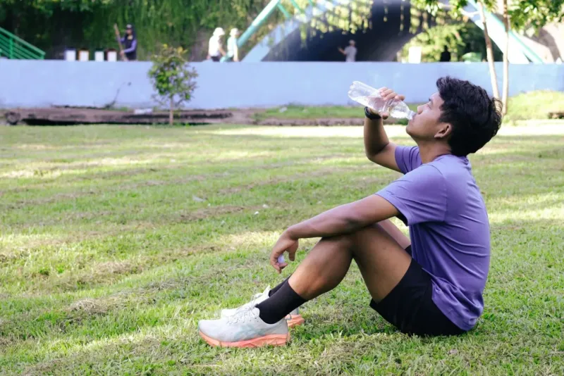 Hardloper drinkt water in het gras na een loop om vocht en elektrolyten aan te vullen