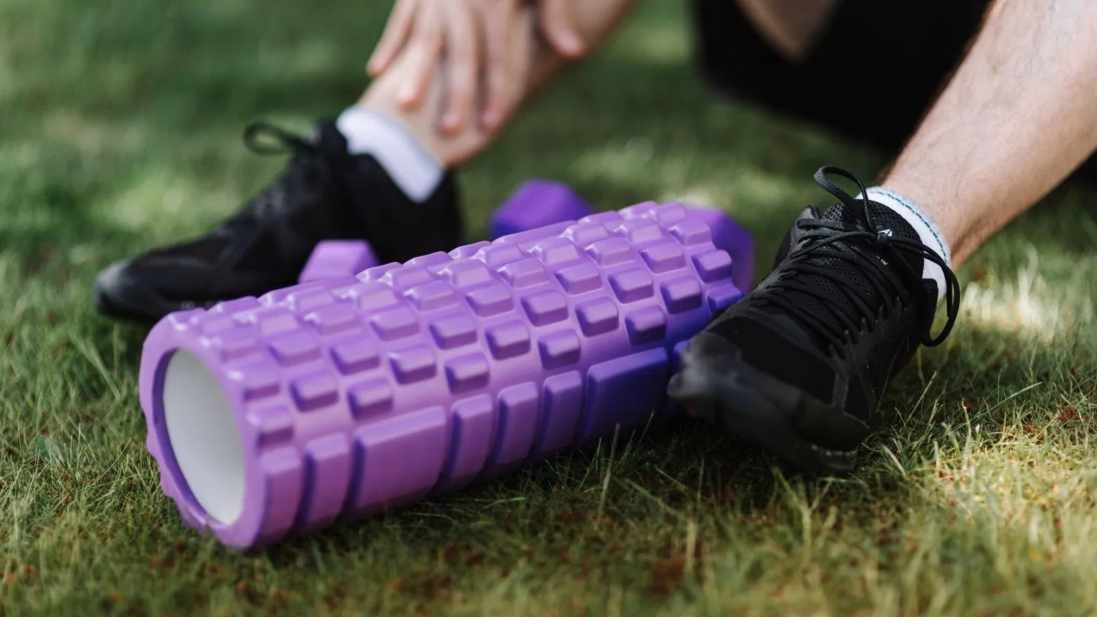 Paarse foam roller en hardloopschoenen op het gras na een training