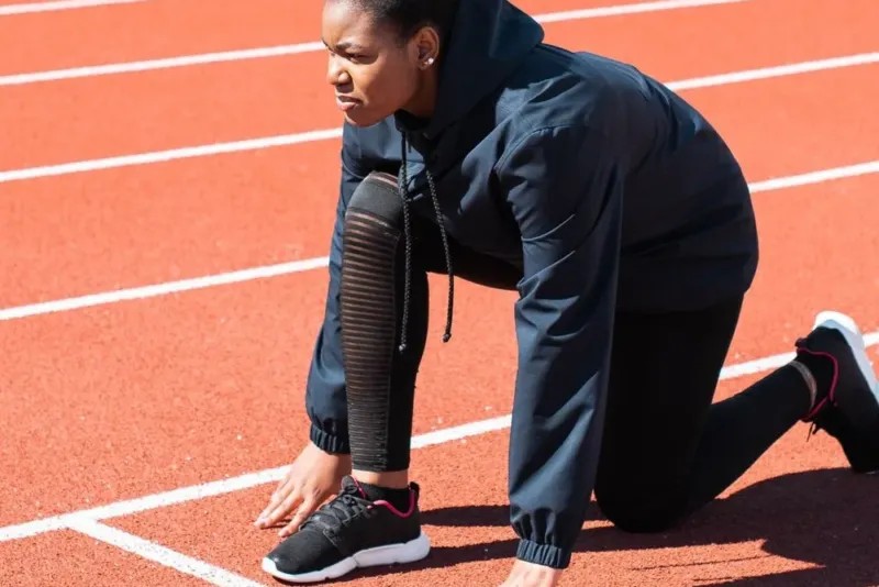 Hardloopster zit geknield op de atletiekbaan voor een blessurevrije training