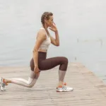 Vrouw doet lunges op een houten steiger bij het water als krachttraining hardlopen