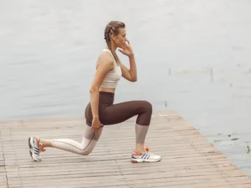 Vrouw doet lunges op een houten steiger bij het water als krachttraining hardlopen