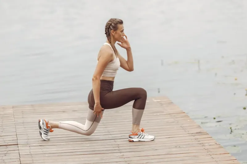 Vrouw doet lunges op een houten steiger bij het water als krachttraining hardlopen