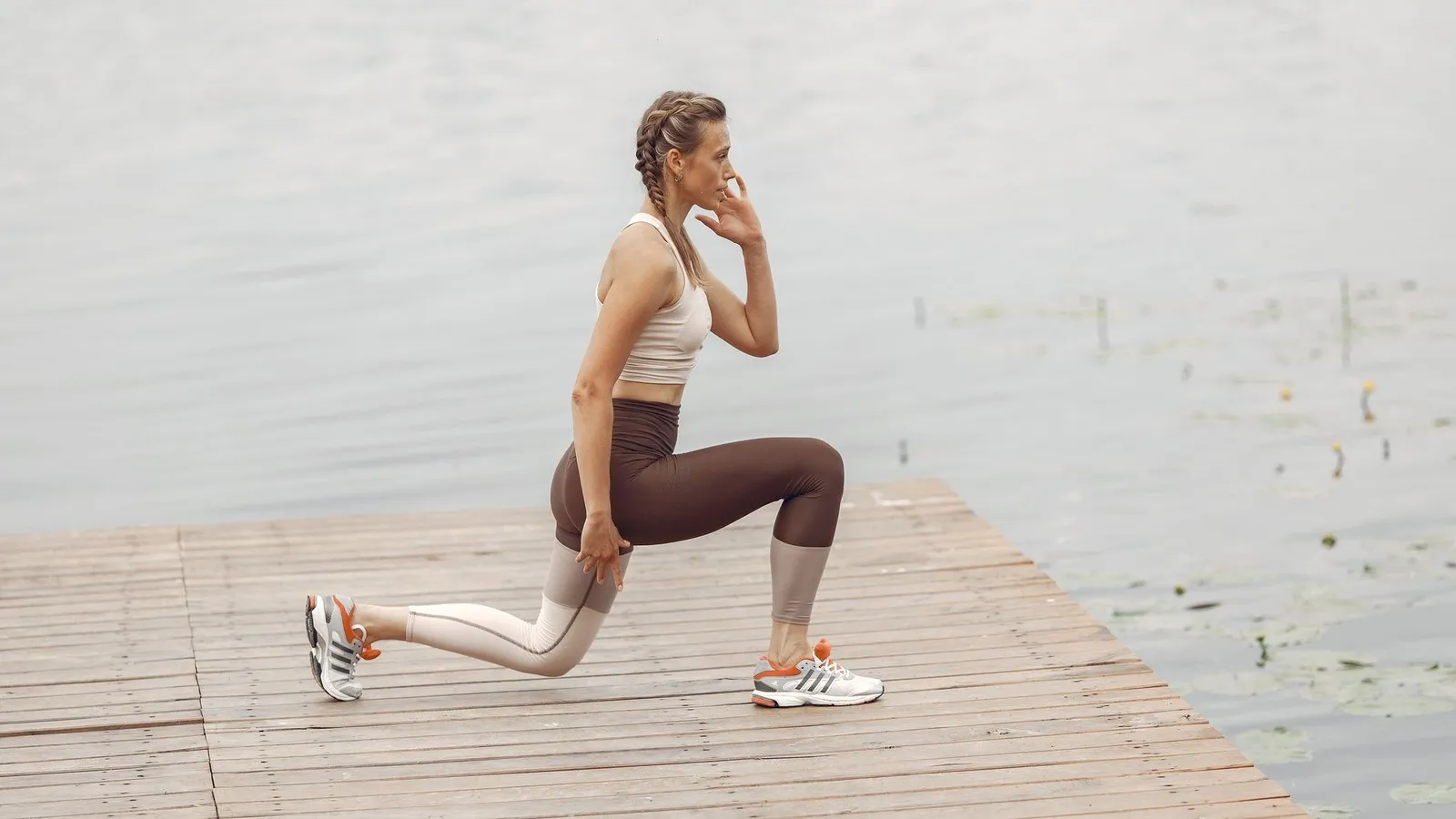Vrouw doet lunges op een houten steiger bij het water als krachttraining hardlopen