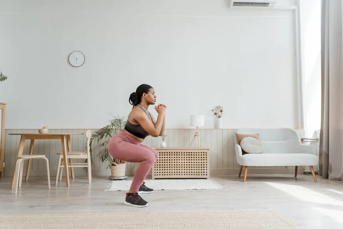 Vrouw doet een squat in de woonkamer als krachtoefening voor hardlopers