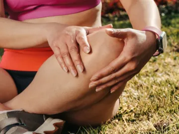 Sportieve vrouw met runners knee houdt haar knie vast terwijl ze op het gras zit