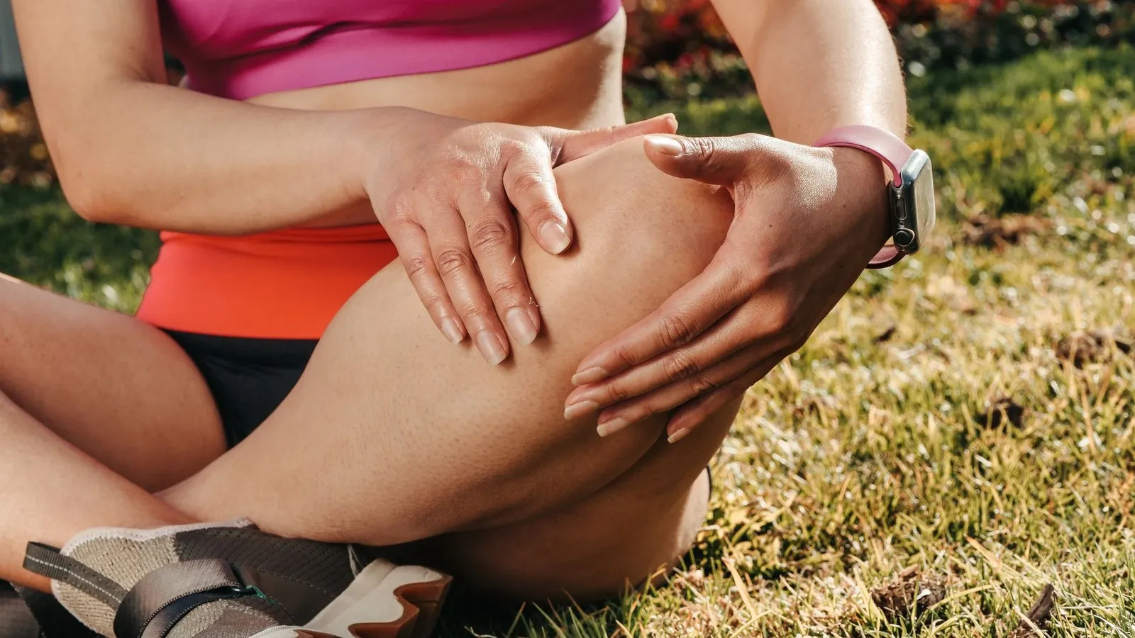 Sportieve vrouw met runners knee houdt haar knie vast terwijl ze op het gras zit