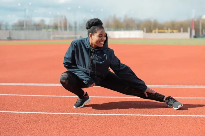 Hardloopster doet een zijwaartse lunge op de atletiekbaan als warming up hardlopen