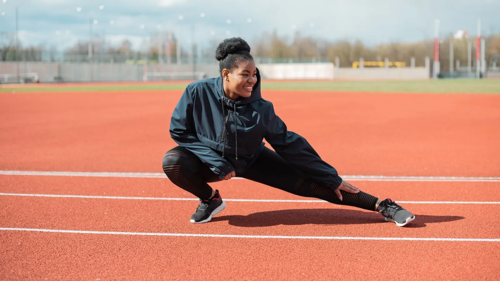 Hardloopster doet een zijwaartse lunge op de atletiekbaan als warming up hardlopen