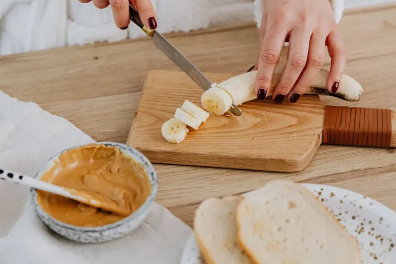 Wat eten voor hardlopen: banaan snijden op een plankje met pindakaas en brood
